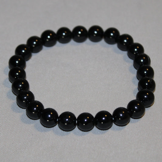 Black Tourmaline crystal with a deep, glossy black surface, resting on a neutral background. Known for its grounding and protective properties, often used for energy cleansing and emotional balance.