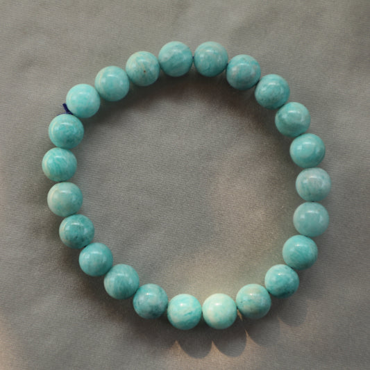 Polished Beads of Amazonite stone made into a bracelet displaying vibrant blue-green shades with white streaks, resting on a neutral background.