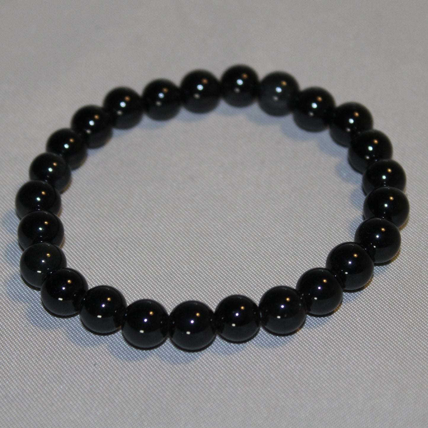 A polished Black Obsidian crystal with a deep, glossy black surface, reflecting light subtly. Known for its grounding and protective properties, this volcanic glass is often used in spiritual practices for energy cleansing and emotional healing. 